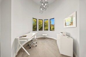A modern office space with a white desk, a white bench, a white reception desk, and a framed picture on the wall.
