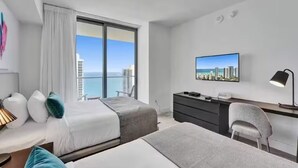 Habitación de hotel con dos camas, un escritorio, una silla, un televisor y un ventanal con vistas a la ciudad.