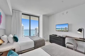 Ein Hotelzimmer mit zwei Betten, einem Schreibtisch, einem Stuhl, einem Fernseher und einem großen Fenster mit Blick auf die Stadt.