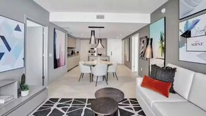 Una sala de estar moderna con un sofá blanco, un comedor con una mesa redonda y una cocina al fondo.