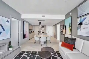 Ein modernes Wohnzimmer mit einem weißen Sofa, einem Essbereich mit rundem Tisch und einer Küche im Hintergrund.