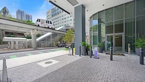 Un edificio moderno con fachada de vidrio, un pasaje peatonal cubierto y un área de estacionamiento con una camioneta blanca.
