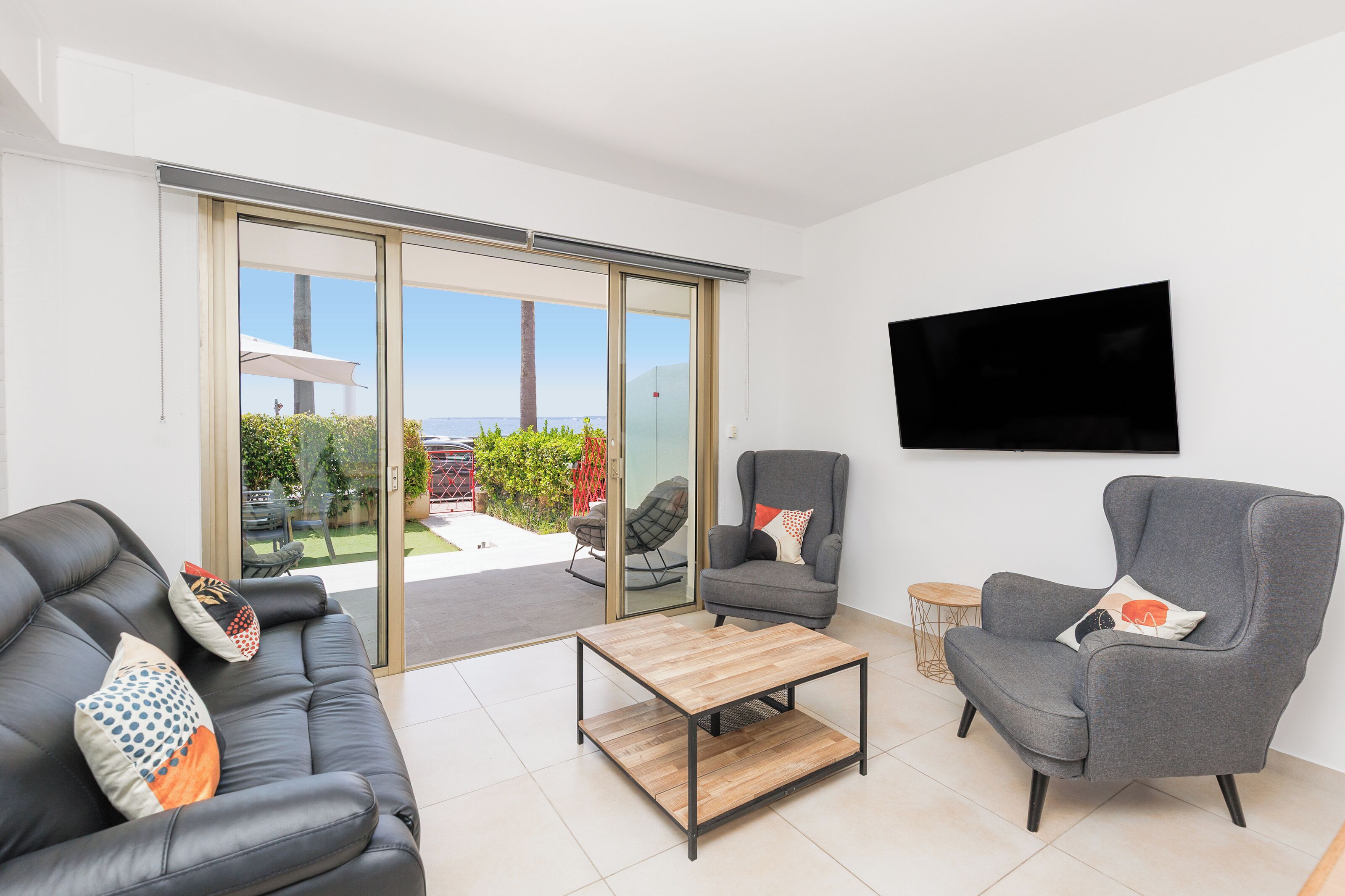 A modern living room with a sofa, armchairs, a coffee table, and a TV mounted on the wall.