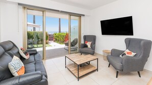 Ein modernes Wohnzimmer mit einer Couch, Sesseln, einem Couchtisch und einem an der Wand befestigten Fernseher.