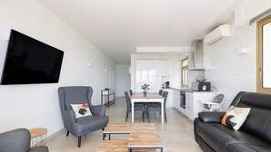 Ein modernes Wohnzimmer mit einem Flachbildfernseher, grauen Sesseln, einem Holztisch und einem schwarzen Ledersofa.