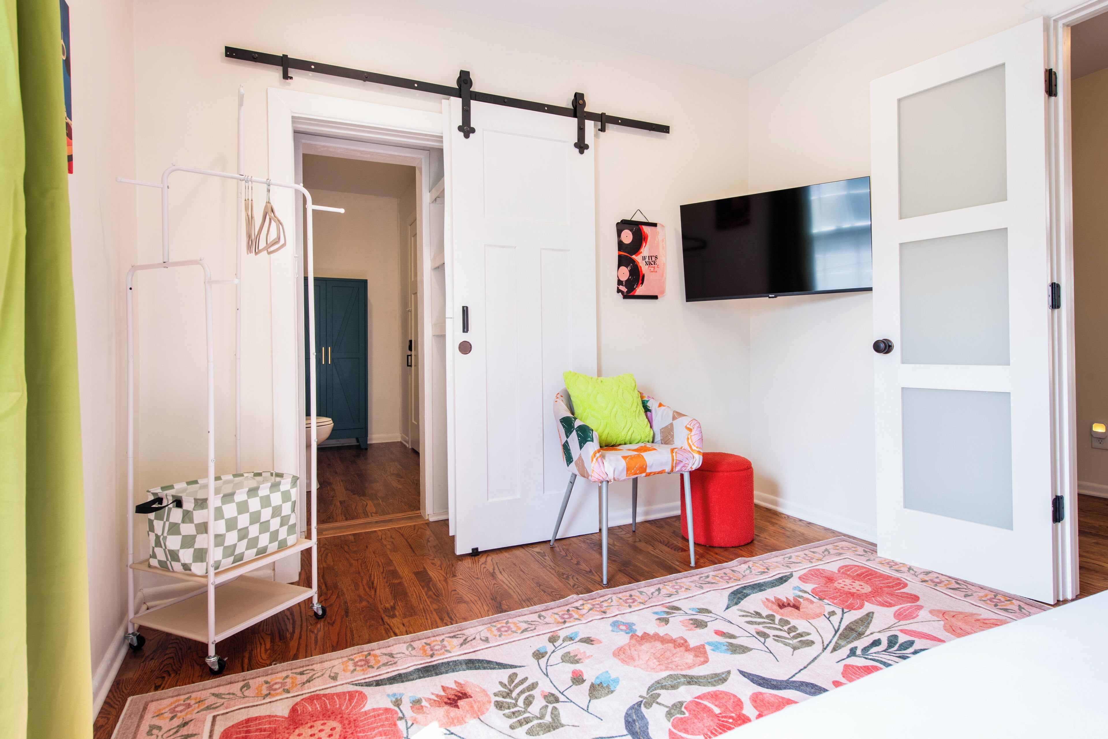 Une chambre avec un berceau, un fauteuil avec un coussin, une télévision et une porte dont les panneaux sont en verre dépoli.