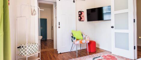 Une chambre avec un berceau, un fauteuil avec un coussin, une télévision et une porte dont les panneaux sont en verre dépoli.