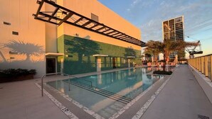 A swimming pool with a glass enclosure, a covered patio area, and a tall building in the background. - 2411 Brand New 1BR - Rooftop Pool, Coworking, Gym, Saun (Miami)