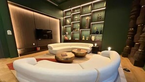 A modern living room with a curved white sofa, two round wooden side tables, and a built-in shelving unit with decorative items. - 2411 Brand New 1BR - Rooftop Pool, Coworking, Gym, Saun (Miami)