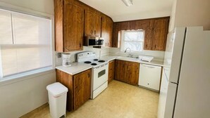 Una cocina compacta con armarios de madera, estufa blanca, un lavamanos y un refrigerador.