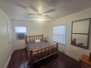 A bedroom with a wooden bed, two windows with blinds, a ceiling fan, and a large mirror on the wall. - Comfortable 2 Bedroom Upper-Level Home in Sugarhouse (Salt Lake City)