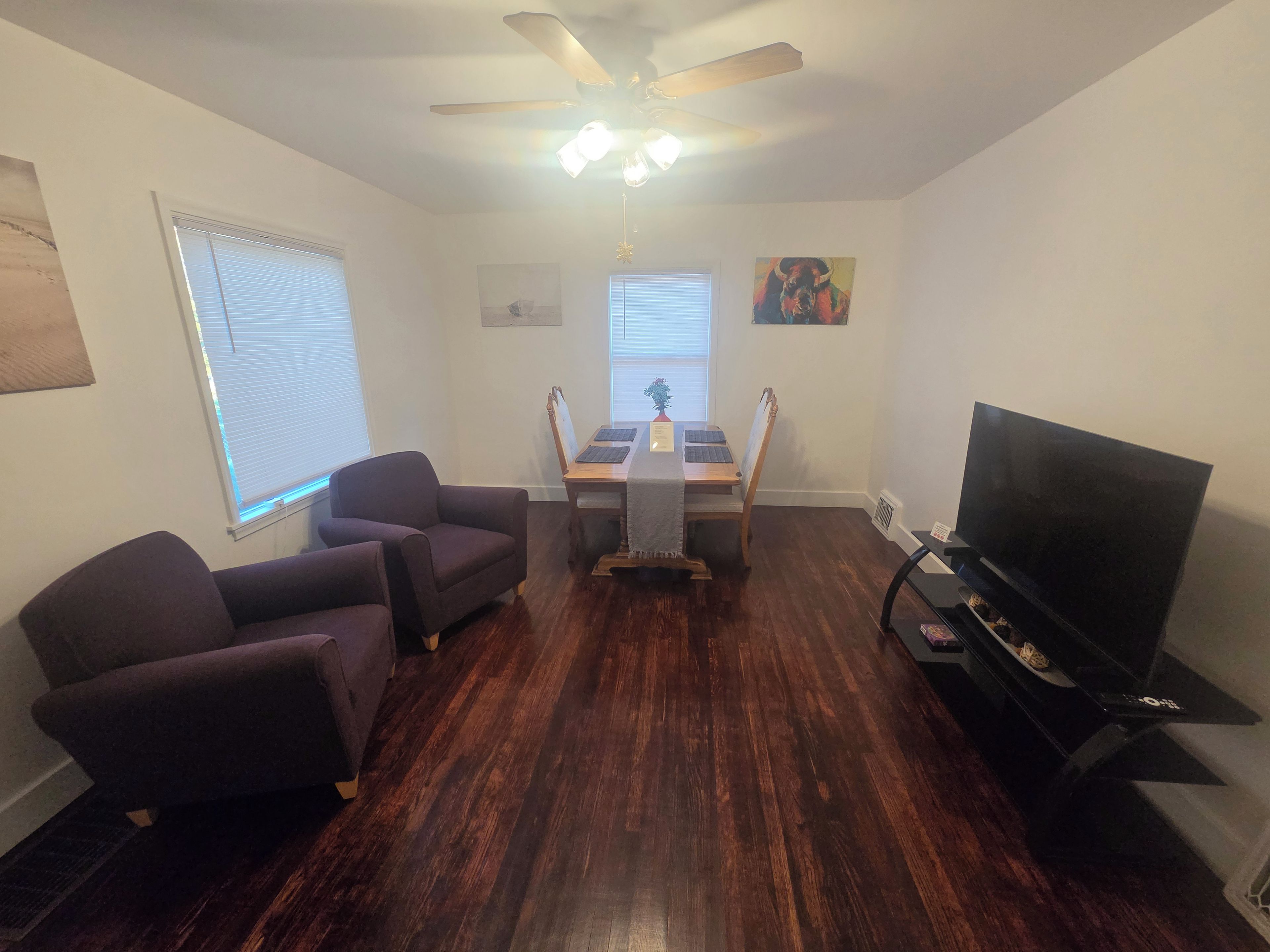 A living room with a dining table, two armchairs, a TV, and a ceiling fan.
