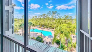 A view from a balcony overlooking a swimming pool surrounded by lush greenery and palm trees. - Family-Friendly 2BR Condo w Resort Pool & Sauna (Winter Garden)