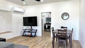Un salon moderne doté d’un téléviseur à écran plat, d’une table à manger avec des chaises, d’un coin cuisine avec une cuisinière et des placards, et d’un ventilateur de plafond.