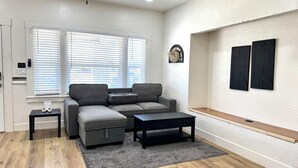 Un salon moderne avec un canapé d’angle gris, une petite table noire, un tapis gris et une étagère en bois.