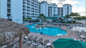 A hotel with multiple floors, a pool area with lounge chairs, and a thatched umbrella. - Penthouse Oceanfront Stay in Cocoa Beach (Cocoa Beach)