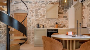 A kitchen with a stone wall, a wooden staircase, and a round dining table with chairs. - Exclusive Heritage Suite Balturio (Kaštel Stari)