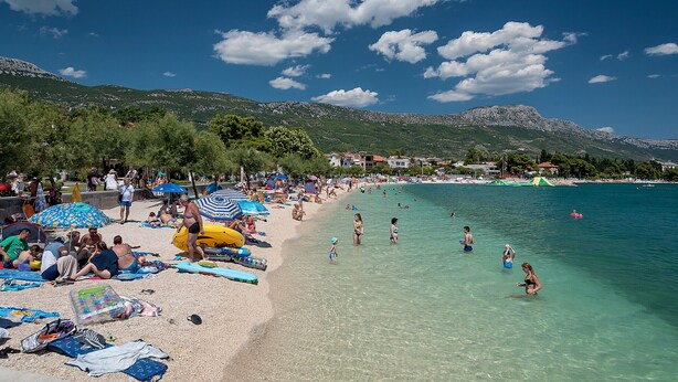 A beach with people sunbathing and swimming, surrounded by mountains. - Exclusive Heritage Suite Balturio (Kaštel Stari)