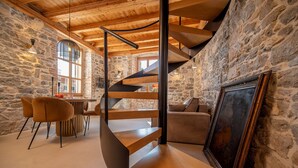 A spiral staircase in a stone-walled room with a dining area and a sofa. - Exclusive Heritage Suite Balturio (Kaštel Stari)