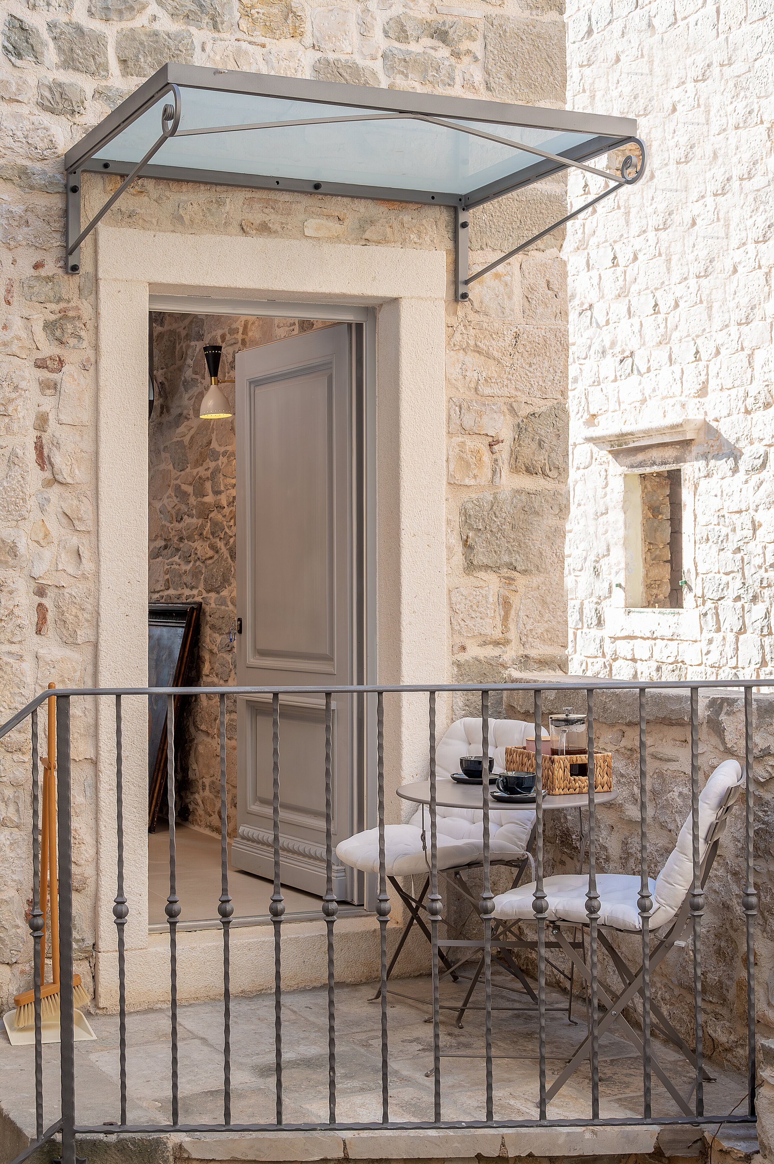 A stone building with a balcony, a table with chairs, and a door.