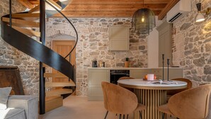 A spiral staircase, a round dining table with chairs, and a kitchen area with stone walls. - Exclusive Heritage Suite Balturio (Kaštel Stari)