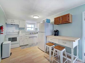 Une cuisine avec des meubles blancs, un réfrigérateur, une cuisinière et deux tabourets.