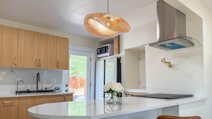 A modern kitchen with wooden cabinets, a white countertop, a hanging light fixture, and a stainless steel refrigerator.