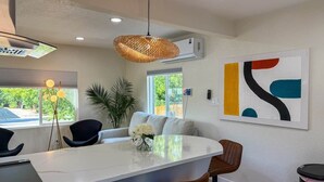 A modern kitchen with a central island, black chairs, a white sofa, and a large abstract painting on the wall.