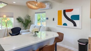 A modern kitchen with a central island, bar stools, a hanging light fixture, and a large abstract painting on the wall.