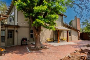 Une maison à deux étages avec un patio couvert, un arbre et un banc.