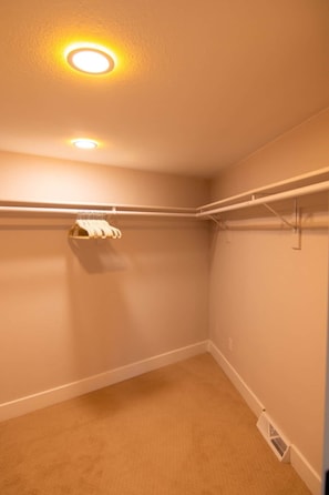 Ein Zimmer mit beigeem Teppich, weißen Wänden, einer Deckenleuchte und einem weißen Kleiderschrank mit Kleiderstange.