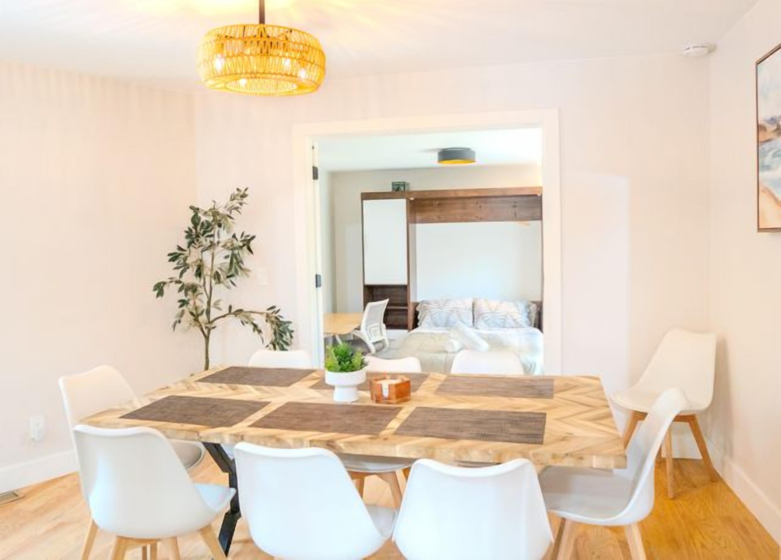 A dining area with a round table, white chairs, and a hanging light fixture.