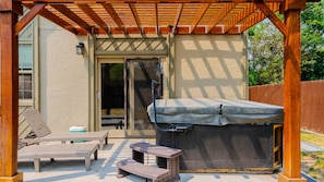 Eine Terrasse im Freien mit überdachter Sitzgruppe, einem Whirlpool und einer Glastür, die zu einem Patio-Tisch und -stühlen führt.