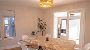 Ein Konferenzraum mit großem Holztisch, weißen Stühlen, einem Blumentopf und einer Pendelleuchte.