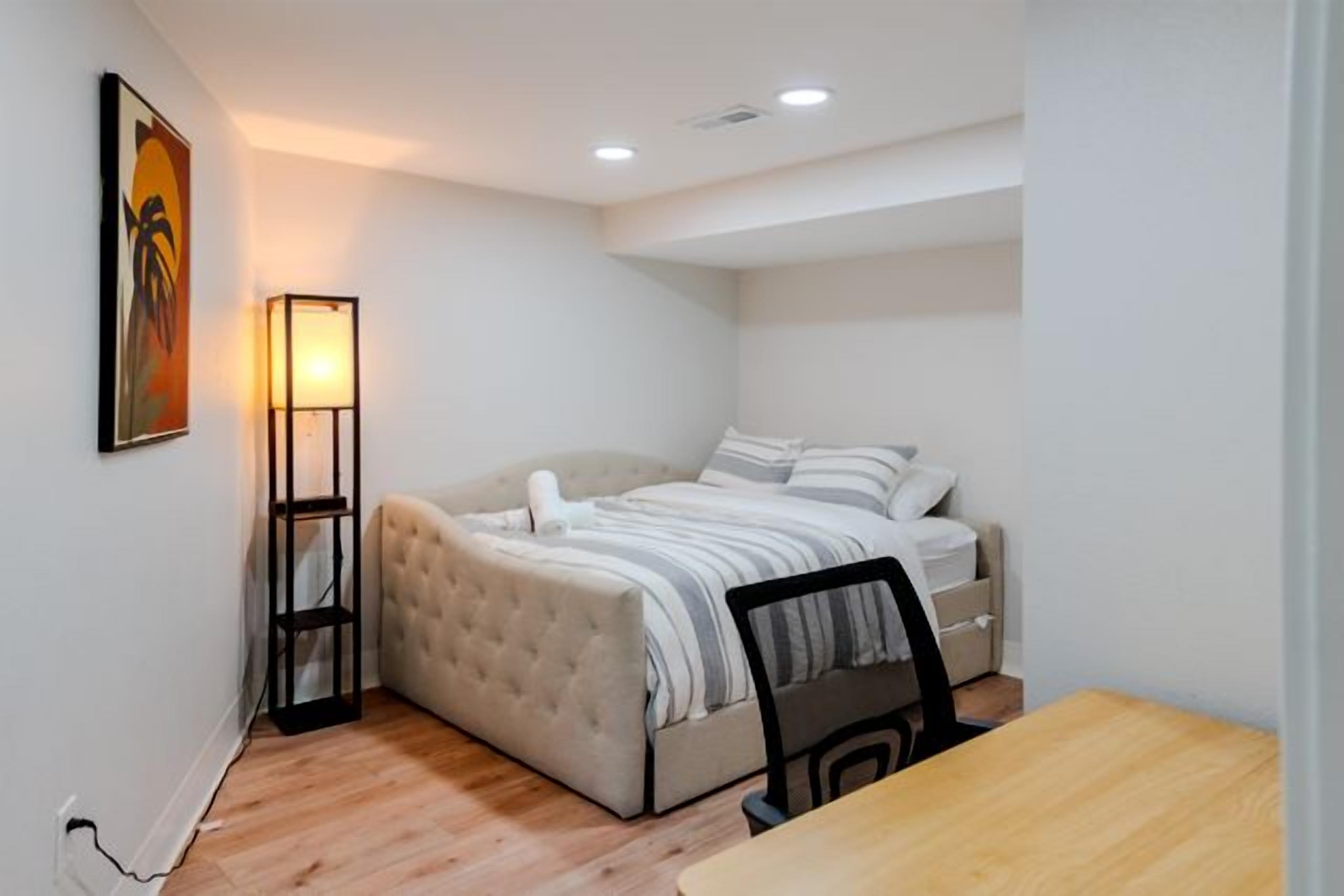 A bedroom with a bed, bedside table, chair, and a floor lamp.