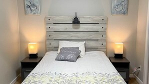 Een slaapkamer met een houten hoofdeinde, twee bedlampen, een bed met een bloemenbedekking en twee vis schilderijen aan de muur.