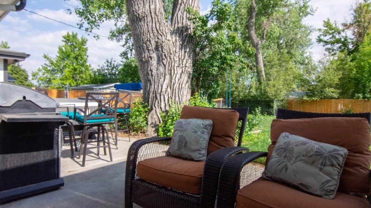 An outdoor patio with wicker furniture, a barbecue grill, and a large tree.