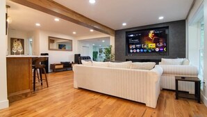 Una sala de estar moderna con un televisor de pantalla plana grande, una zona de comedor de madera y un sofá.