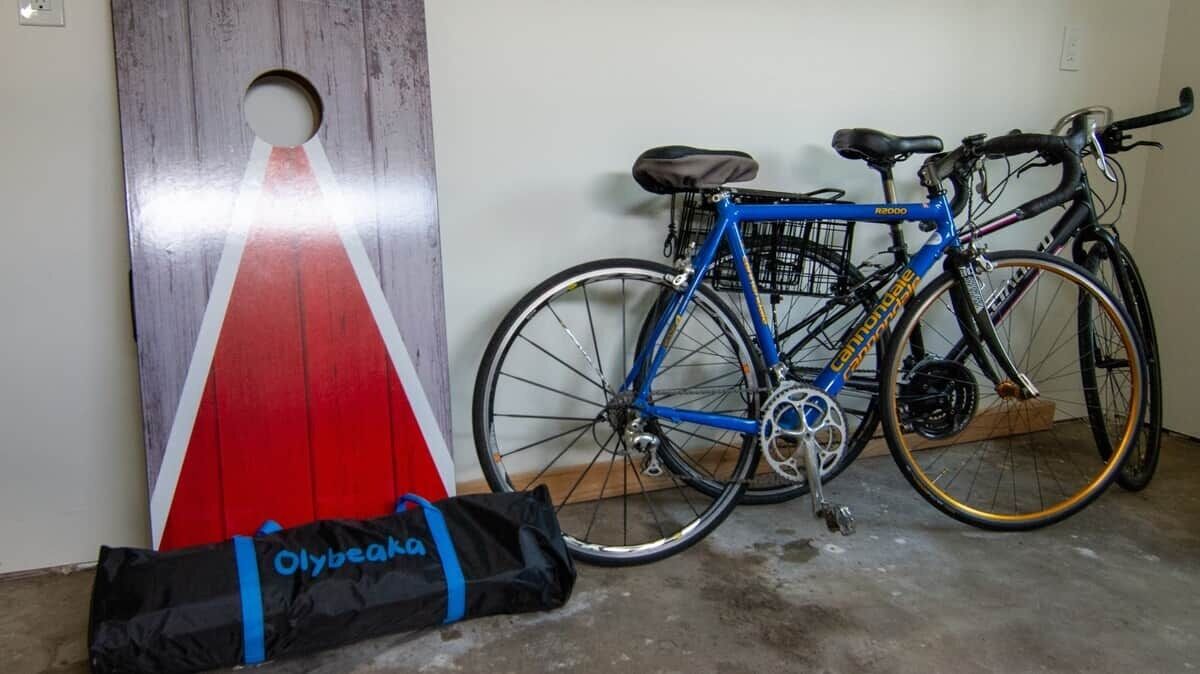 Un vélo bleu, un sac noir orné du mot « Olybeak », et un objet rouge et blanc appuyé contre un mur.