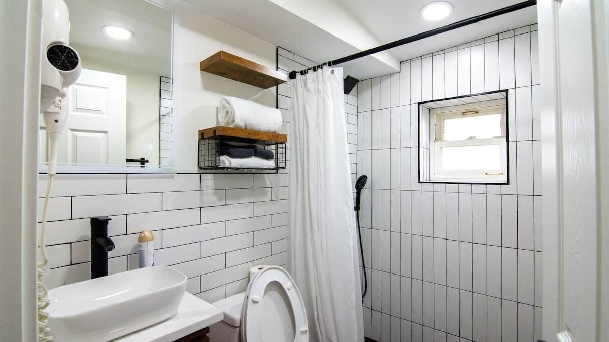 A bathroom with a white sink, a toilet, a shower curtain, a towel rack with towels, a mirror, and a window.