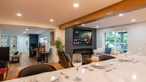Una sala de estar moderna con chimenea, un comedor con mesa para dos personas y un televisor montado en la pared.