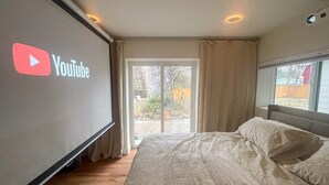 Un dormitorio con una cama, un ventanal grande y el logo de YouTube en la pared.