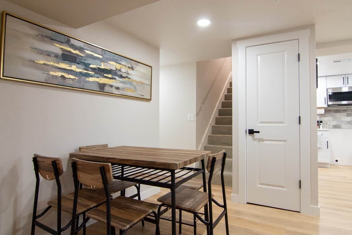 Un espace repas avec une table et des chaises en bois, un escalier et une cuisine en arrière-plan.