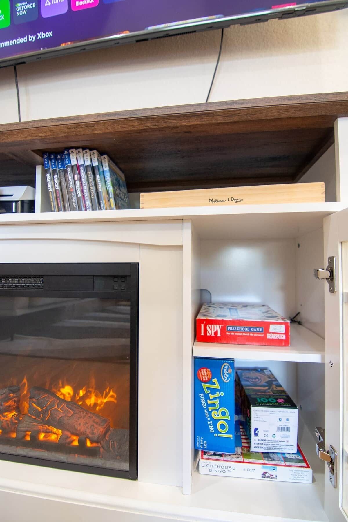 A fireplace with logs, a shelf with video game cases, and a box of 'I Spy' preschool game.