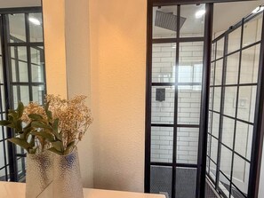 A bathroom with a tiled wall, a glass shower enclosure, and a vase with dried flowers on a counter. - Studio with Private Bathroom (Englewood)