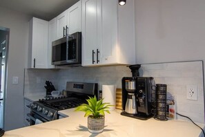 A modern kitchen with white cabinets, a stainless steel stove, a coffee maker, and a potted plant on the counter. - Patio getaway 5 min from downtown (Denver)