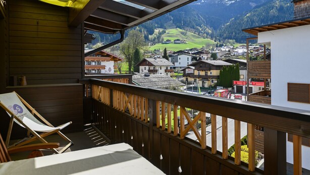 A balcony with a view of a mountain town, wooden railings, and a lounge chair. - Ski & Golf Suite 25: balcony, Maiskogel View (Kaprun)