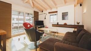 A modern living room with a brown sofa, a glass coffee table, a red chair, a TV, and a wooden ceiling. - Ski & Golf Suite 25: balcony, Maiskogel View (Kaprun)