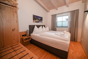 Ein Schlafzimmer mit einem hölzernen Bett, einem Nachttisch, einem Fenster mit Vorhängen und einem Bild an der Wand.