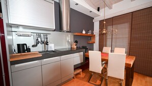 A modern kitchen with a built-in dishwasher, a stainless steel range hood, and a dining area with a wooden table and chairs. - Ski & Golf Suite 25: balcony, Maiskogel View (Kaprun)